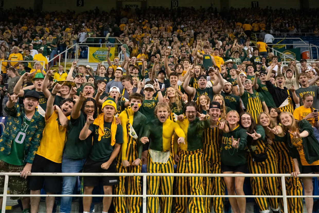 NDSU football fans wearing green and gold cheer in a stadium