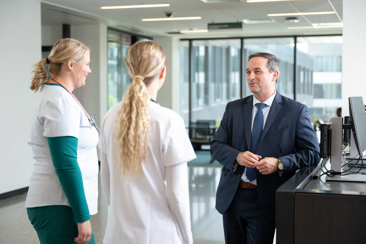 a man in a suit talks to two students in nursing attire
