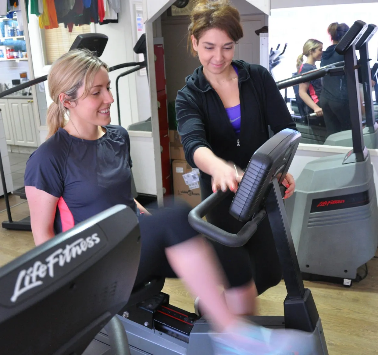 Fitness coach showing a client how to adjust machine settings in a workout room