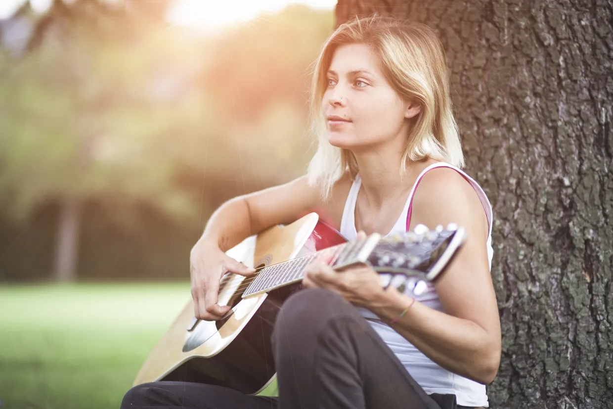 Woman sitting next to a tree, playing guitar
