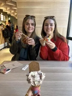 three students sitting at a table with dessert in their hands