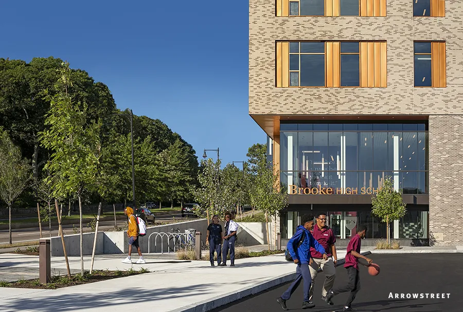Exterior rendering of a modern building with people walking out front on sidewalk and parking lot.