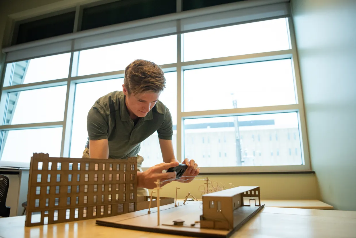 Architecture student working on a model-sized structure sitting on top of table.