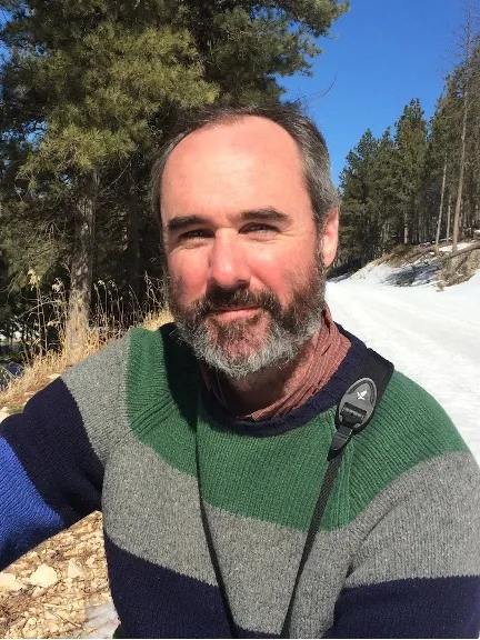 Tim looking confidently at camera with trees in the background on a sunny day.