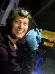 Mandy Guinn wearing a head lamp and blue gloves while smiling confidently at camera.