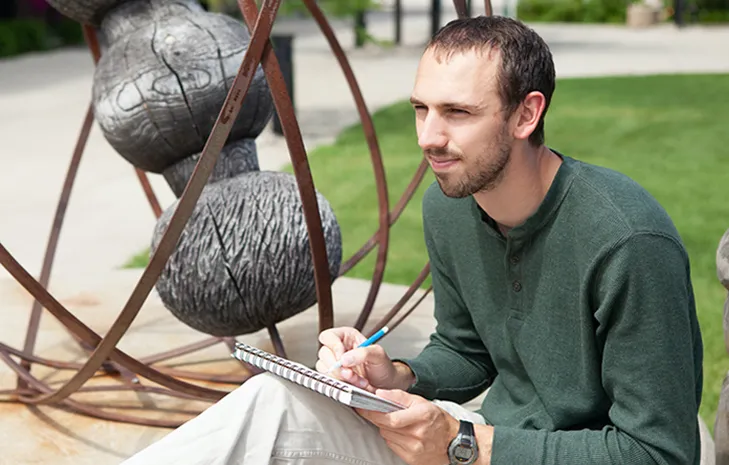 Matthew Neururer sitting with pencil and notebook while looking confidently in the distance. 