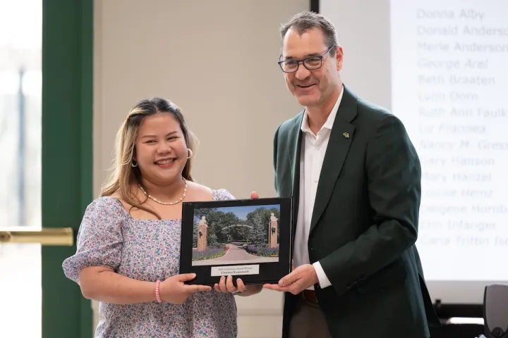 NDSU doctoral student Chutikun “Chuti” Kanjanaruch stands next to NDSU President David Cook while they both hold the Gunkelman Award and pose for a photo.