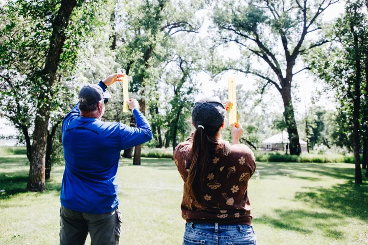 Two educators use a ruler to measure the height of a tree