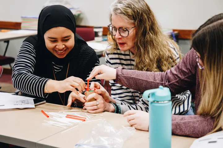 A group of women work together to put straws into a toilet paper roll to model the parts of a tree