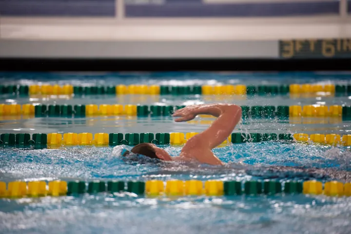 male in wellness center lap pool swimming between green and yellow lane ropes