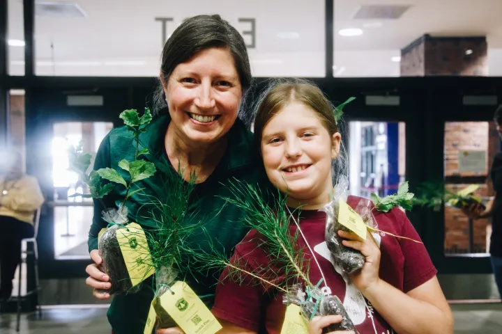 A woman and her daughter smiling while holding tree seedlings