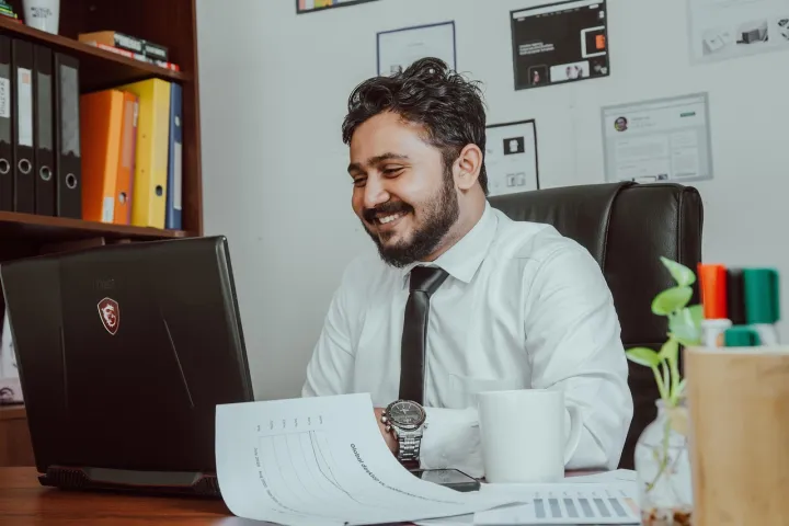 Man working in an office looking at computer screen while papers and coffee cup are on his desk. 