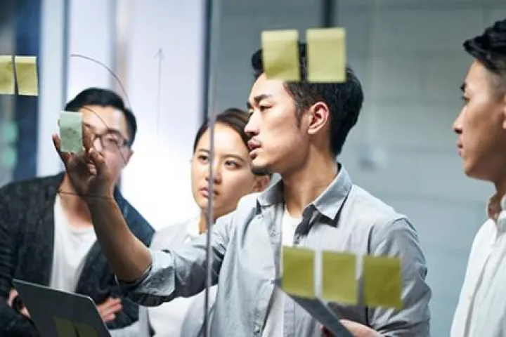 Group of workers at a glass window with post it notes brainstorming
