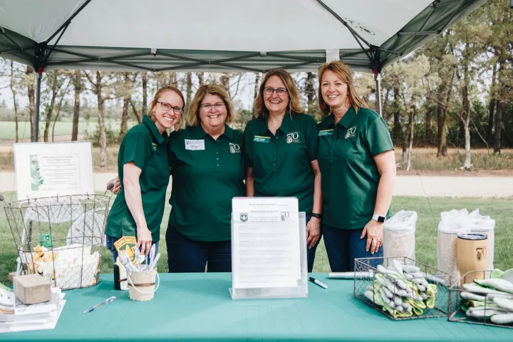 Four women in matching green polos smile together in front of a booth with a canopy overhead.
