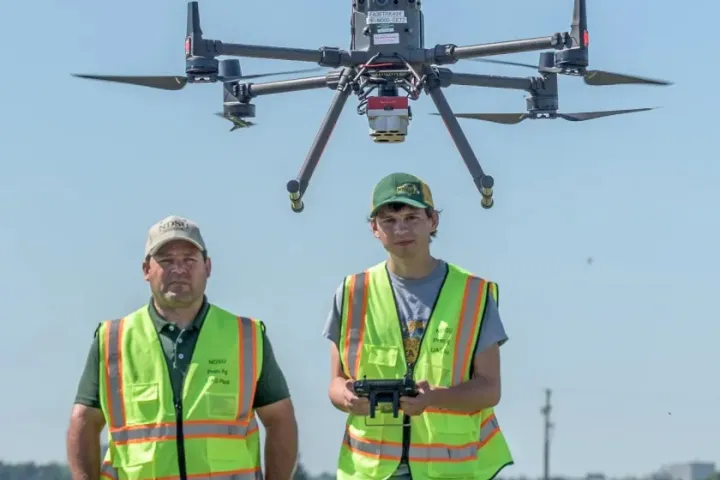 Two researchers stand in front of a flying drone