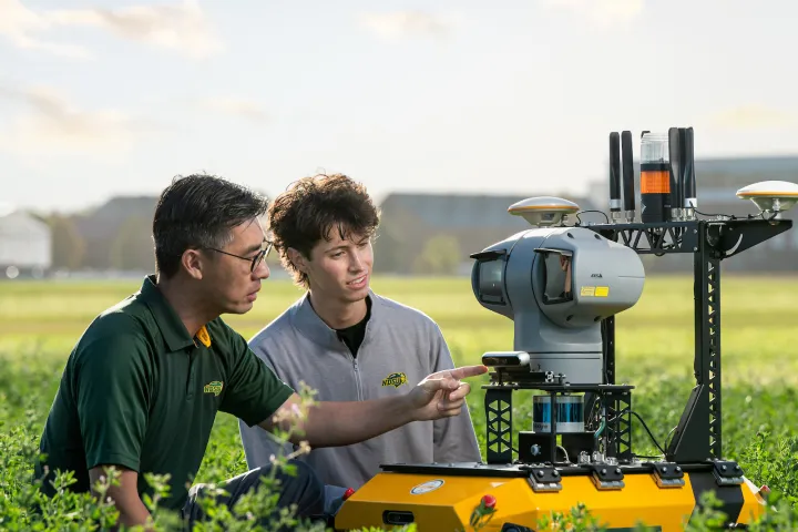 Professor teaching a student next to a piece of equipment in a field