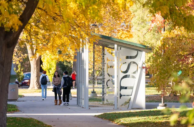 students waiting by bus shelter on campus on a fall day