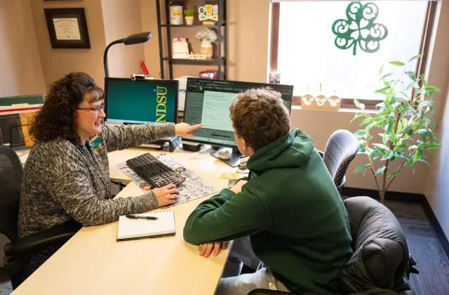 Patti Seidler, an NDSU professional advisor, sits at her desk with a student.
