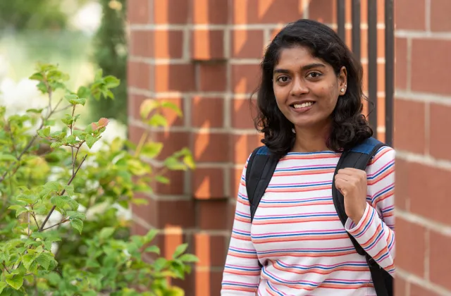 Sri poses outside by building with backpack