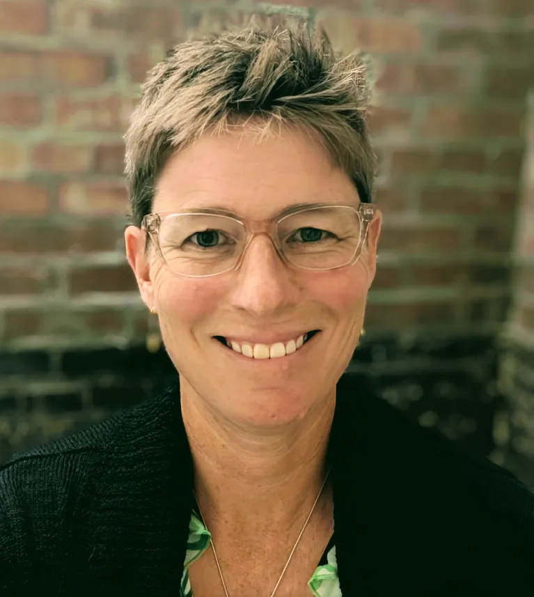 A women with short blond hair, with wire frame glasses.
