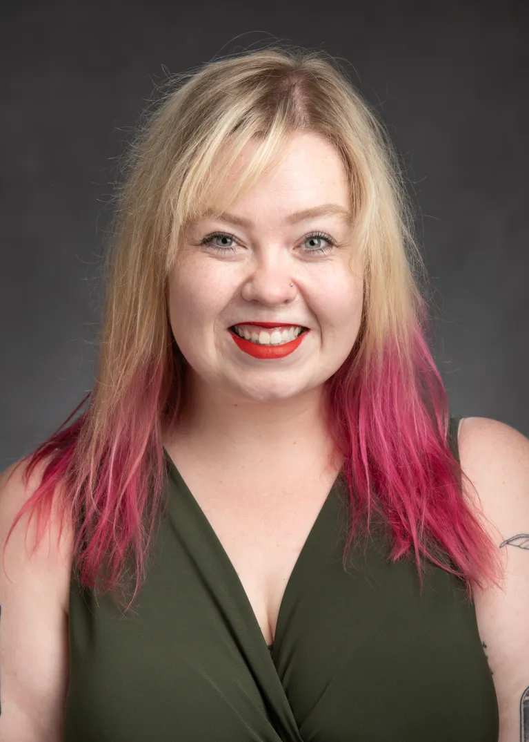 A women with long blond hair with pink ends. Wearing red lipstick and a green shirt