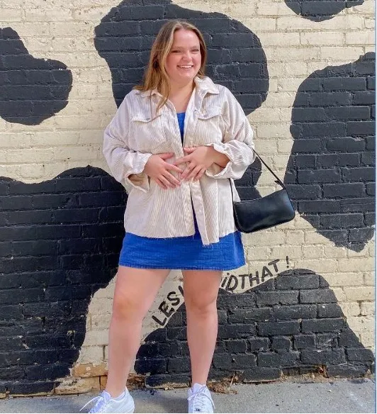 Student smiling confidently while standing in front of a brick wall painted in cow print.