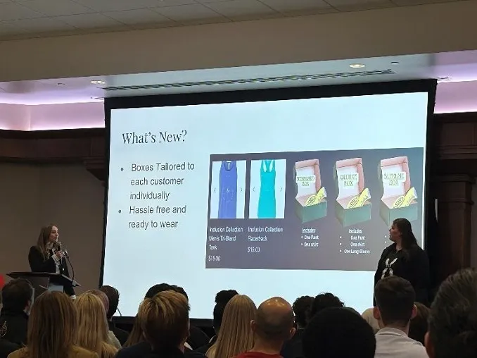 Student presenting at front of room while looking at screen.