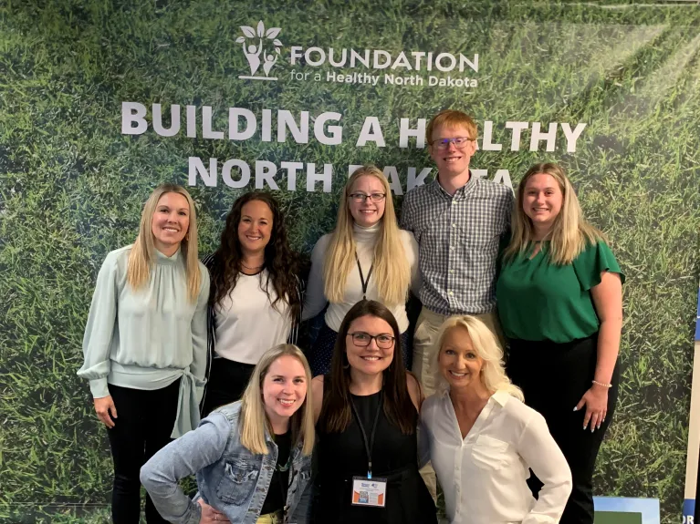 Eight CIRE staff members and collaborations posing in front of a backdrop that says "Building a healthy North Dakota"