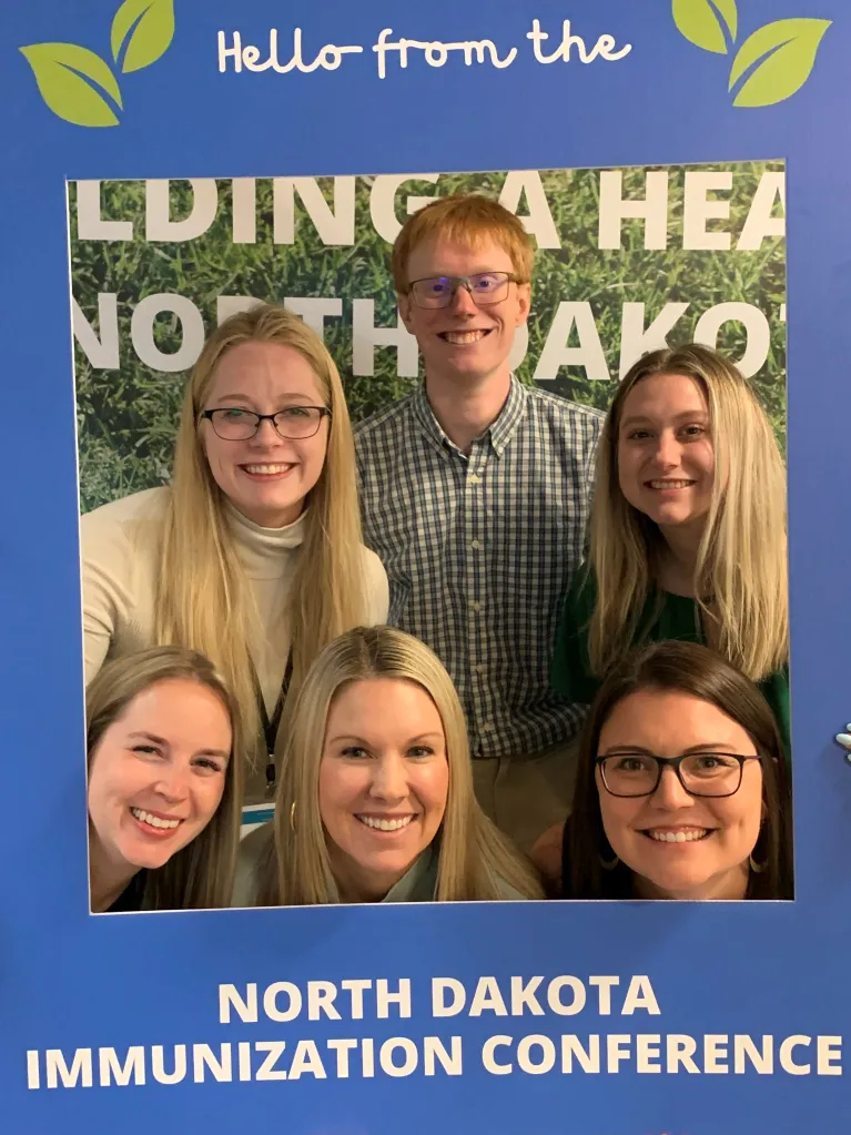 Six CIRE staff members posing inside a frame that says "Hello from the North Dakota Immunization Conference"