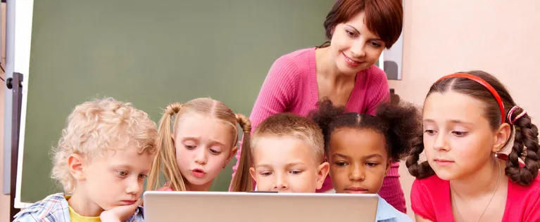 Female teacher showing five elementary students content on a computer.