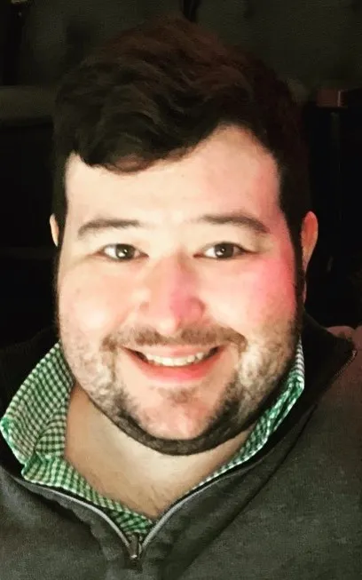 A headshot of Don Johnson, a White man with dark brown hair and a beard, wearing a green checked shirt and pullover.