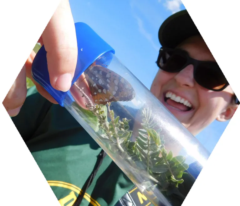 Person smiling and holding a butterfly in a tube