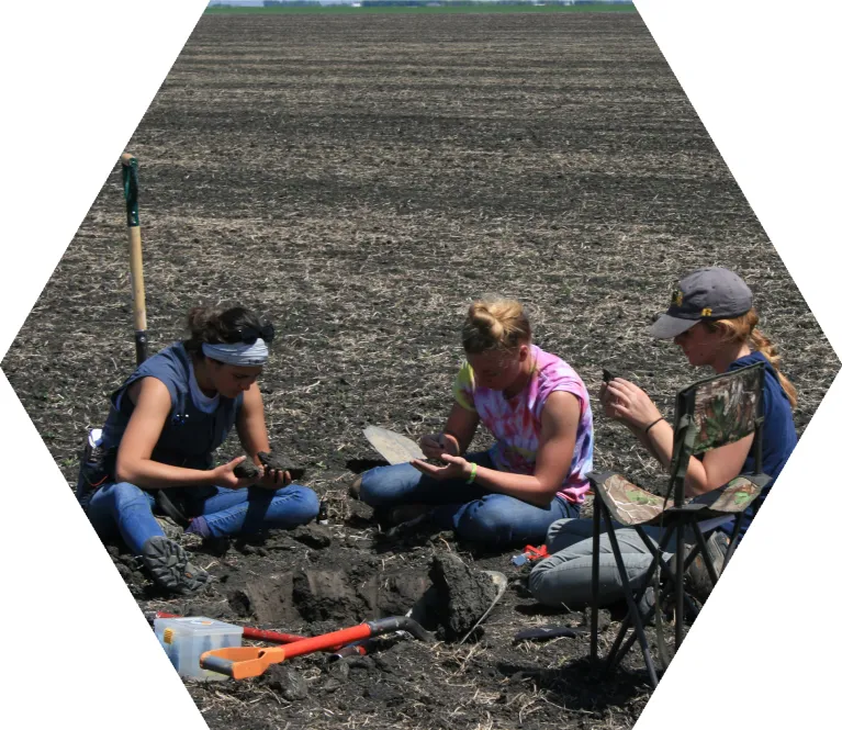 Three people crouched in a field examining the soil