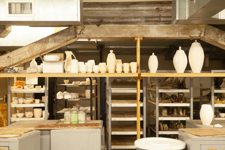 Shelves with dried clay pots of all shapes and sizes, tables and equipment in ceramics studio.