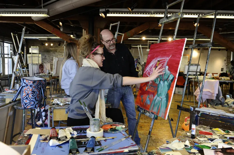 Faculty works with student in painting studio.