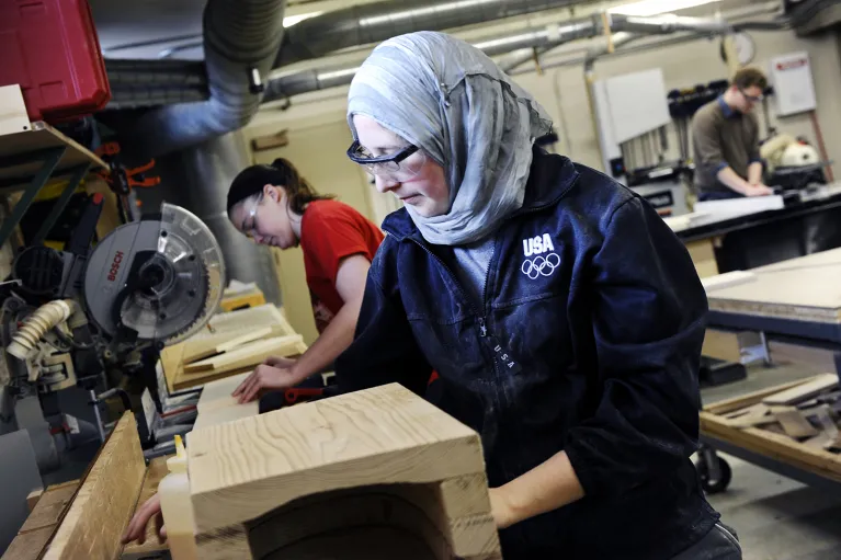 Student wearing protective eyeware while working with wood in woodship.