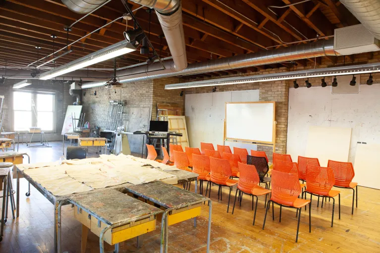 3 rows of chairs sitting between tables at back and white board at front of room.