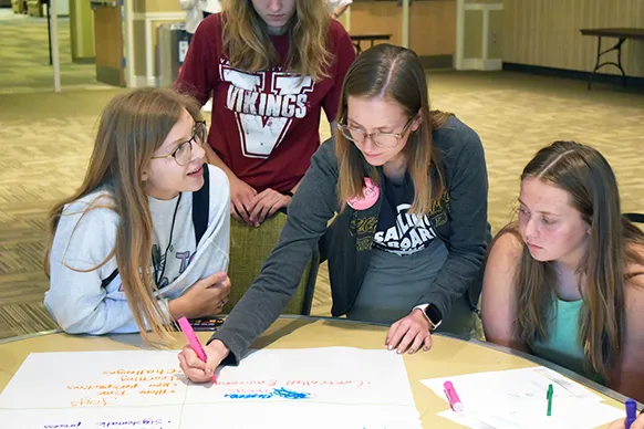 4-H kids gathered around a table writing on large sheets of paper
