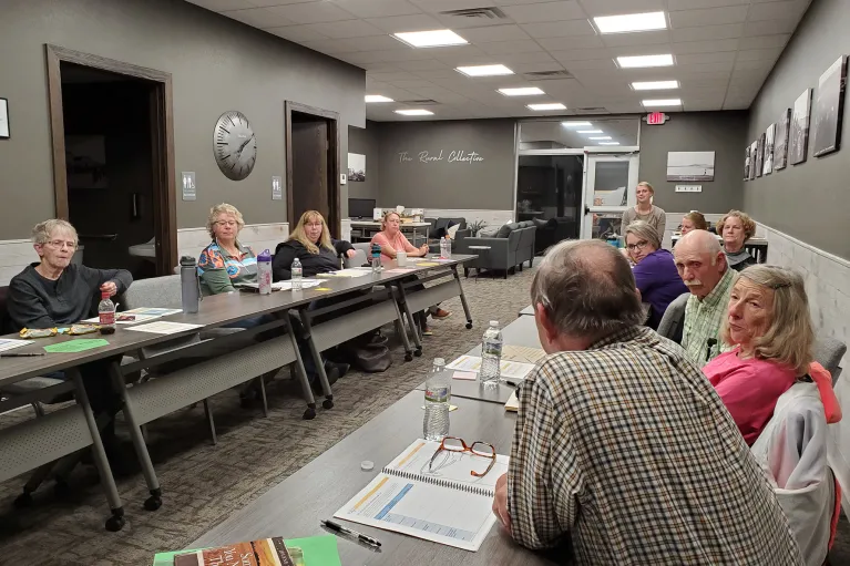 Several people sit at two long table facing each other in a conference room