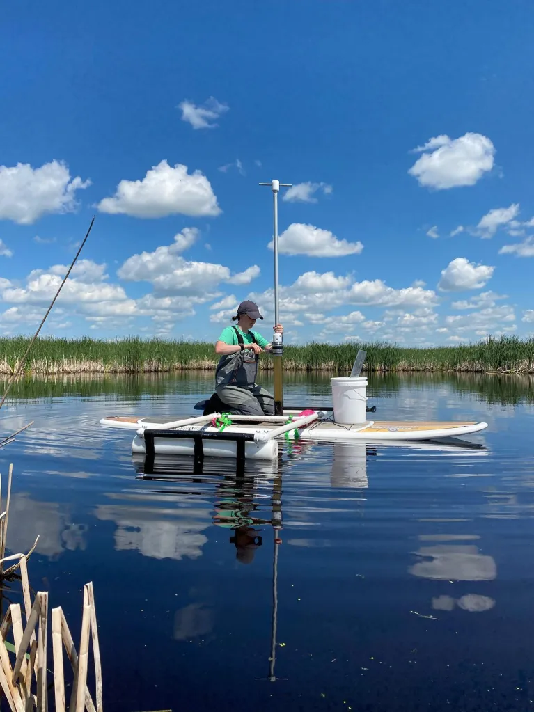 Christine Cornish sitting on a paddle board preparing a freshly collected sediment core for extrusion